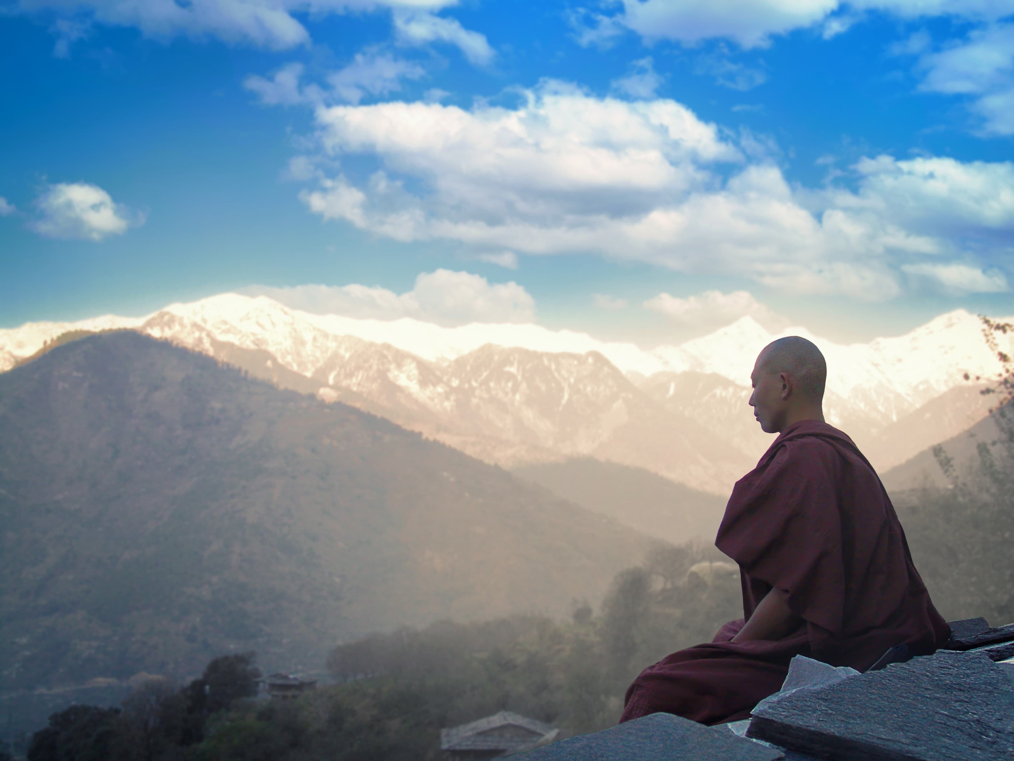 A monk in meditation on a ledge above a Himalayan valley, snow peaks beyond at first light