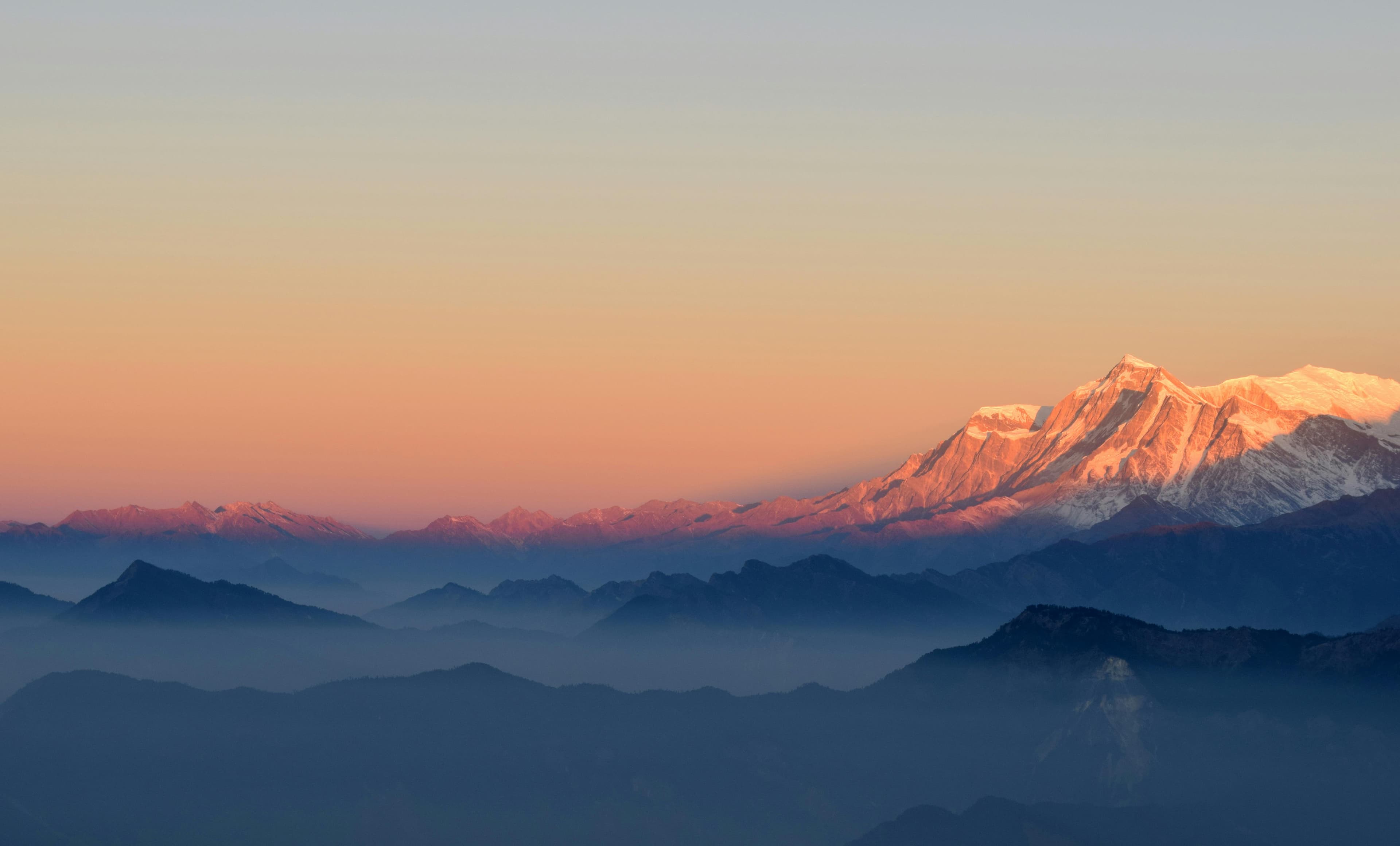 Snow-dusted Himalayan peaks catching the last light above layered, mist-filled ridges
